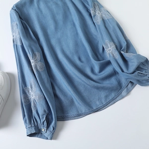 Détail de la broderie florale blanche sur les manches en jean bleu clair à revers