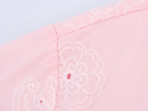 Détail de broderie florale blanche élégante sur une chemise rose clair à manches longues