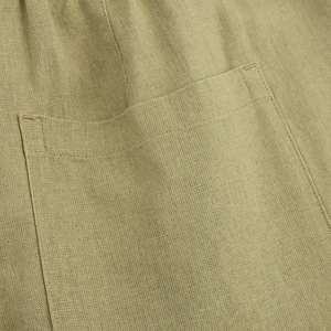 Detailed macro view of olive linen fabric texture and reinforced stitching on a patch pocket