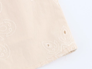 Detail of cream sleeveless dress featuring paisley eyelet embroidery and scalloped edges