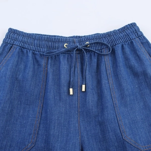 Close-up of drawstring waist on dark blue washed denim joggers with gold metal tips