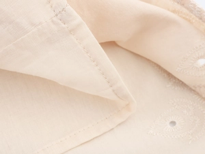 Macro view of light beige eyelet embroidery fabric with precision double stitching