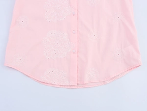 Détail de l'ourlet de chemise rose avec broderie florale blanche et boutons délicats