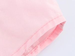 Détail du poignet d'une chemise rose clair avec coutures nettes et broderie florale blanche