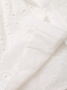 Close-up of intricate white eyelet embroidery and matching button on cotton fabric