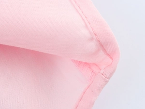 Gros plan sur le tissu brodé rose montrant la texture fine et les détails de couture