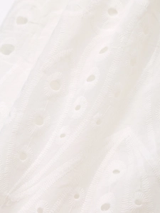 Macro shot of white eyelet embroidery fabric with geometric floral cutouts on mini dress
