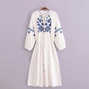 Détail de la broderie florale géométrique bleue sur une robe bohème blanche