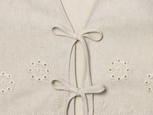 Detail der beige Leinenweste mit Augenbestickung und Schnürung an der Vorderseite