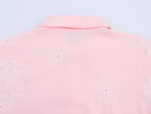 Détail d'une chemise rose à manches longues avec broderie anglaise florale blanche