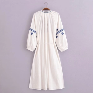 Détail de la broderie ethnique bleue sur une robe longue bohème blanche à pompons