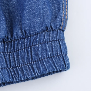 Detailed close-up of elastic cuffs on blue denim joggers with orange double stitching