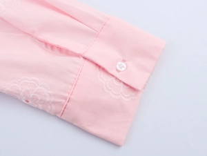 Détail du poignet de chemise rose avec broderie florale blanche et bouton translucide