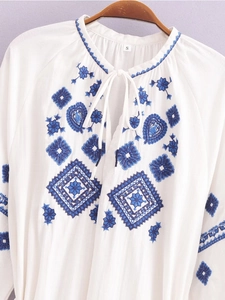 Robe blanche brodée boho avec col en V, glands et manches longues sur cintre