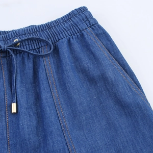 Close-up of drawstring waist on blue denim joggers with gold metal eyelets and stitching