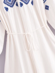 Détail de la broderie florale bleue et cordon de serrage sur robe blanche en coton