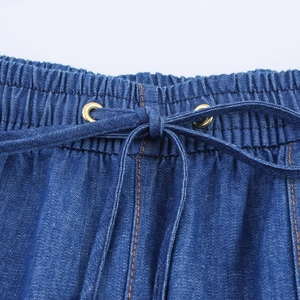 Close-up of elastic high waist with drawstring and orange stitching on denim pants