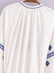 Détail de la broderie ethnique bleue sur l'encolure et les manches d'une blouse blanche