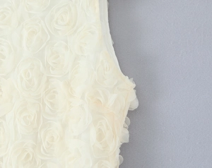 Detail of 3D rose appliqué fabric on a white sleeveless dress with intricate floral texture