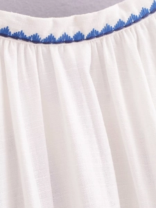 Gros plan détaillé de la broderie bleue sur robe blanche en coton avec franges
