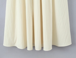 Detailed close-up of light beige maxi dress fabric with fine vertical pleated texture