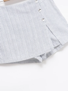 Détail d'une jupe-culotte à rayures bleues avec une rangée de boutons blancs polis