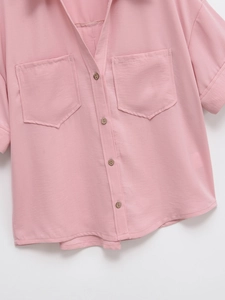 Detailed close-up of pink short-sleeve shirt fabric with wooden buttons and pockets