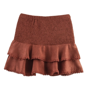 Detail of high waist elastic smocked waistband and layered ruffle trim on rust mini skirt