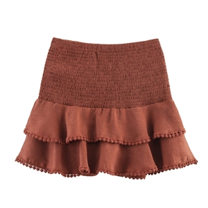 Detail of smocked elastic waistband and ruffled hem with pom-pom trim on brick red skirt