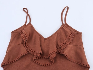 Detail of red-brown camisole featuring layered ruffles and delicate pom-pom trim edges