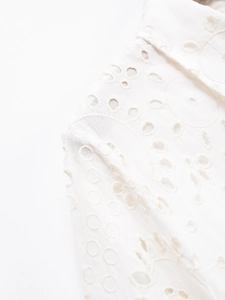Detailed macro view of white cotton eyelet embroidery and stitching on the dress shoulder