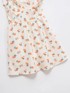 Flat lay of a summer backless dress with orange fruit print on a beige background
