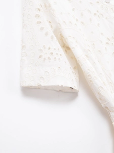 Close-up of white cotton eyelet embroidery and intricate floral needlework on the sleeve