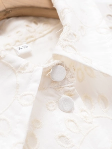 Detail of white cotton shirt dress showing eyelet embroidery and fabric buttons