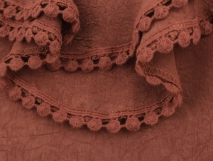 Close-up of terracotta pleated fabric featuring delicate pom-pom lace trim details