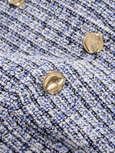 Macro shot of blue and white tweed fabric texture with decorative gold embossed button