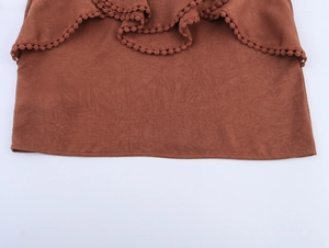 Close-up of textured rust-red fabric with layered ruffles and delicate pom-pom trim details