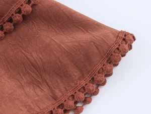 Close-up of brick red pleated fabric with pom-pom trim detail and bohemian texture
