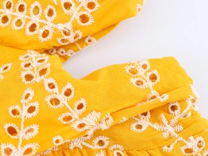 Dettaglio di tessuto giallo con ricamo floreale bianco e raffinati motivi traforati