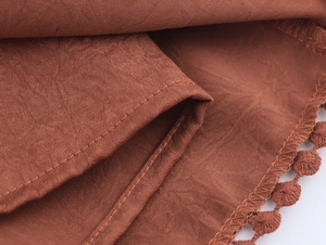 Macro detail of rust red woven fabric featuring delicate pom-pom lace trim and stitching
