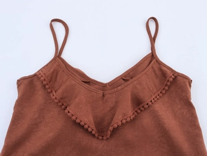 Detail of V-neck brown tank top with lace trim and pompom ruffles on pleated fabric