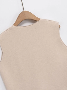 Gros plan du gilet en maille beige montrant des coutures fines sur un cintre en bois