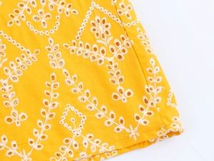 Dettaglio del tessuto dell'abito estivo giallo con ricami floreali bianchi e trafori