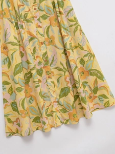Détail d'une jupe jaune à fleurs oranges avec des boutons marron sur le devant