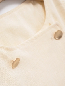 Detailed macro view of cream cotton-linen vest fabric and matte gold buttons