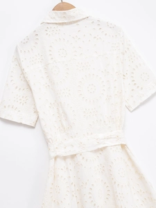 Detailed close-up of white cotton eyelet embroidery and floral cut-outs on dress fabric