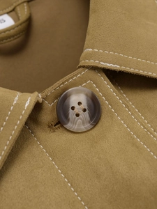 Détail macro d'une veste en suédine avec surpiqûres contrastées et bouton marbré
