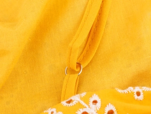 Dettaglio vestito giallo con anello metallico sulla spallina e ricamo a margherita