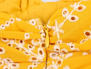 Vista macro del tessuto giallo in cotone e lino con ricamo a margherita e cerniera invisibile
