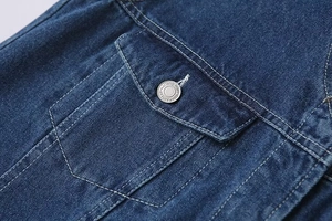 Détail macro d'une poche en denim bleu foncé avec un bouton en métal argenté gravé
